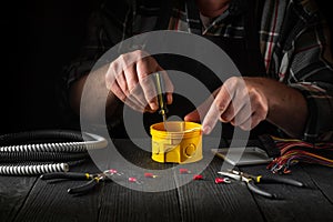 Close-up of hands of a master electrician during work. Installing a cable or wire to yellow junction box. Free advertising space