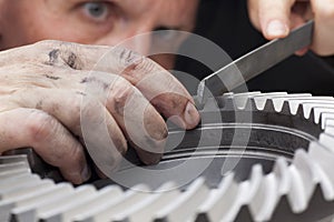 Close-up of hands of a mechanic repairing a cog wheel with a rasp photo