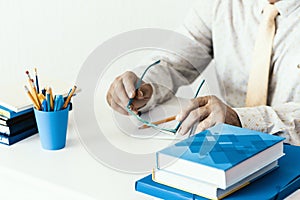 Close-up of hands middle-aged man in white shirt typing on keyboard laptop computer, holder with pencils and pens, stack of books