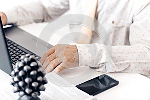 Close-up of hands middle-aged man in white shirt and yellow tie typing on keyboard laptop computer, concrete holder with pencils