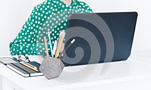 Close-up of hands middle-aged woman in green blouse typing on keyboard laptop, concrete holder with pencils and pens, notebook,