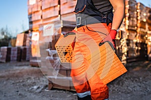 Close up on hands and midsection of unknown man construction worker taking orange hollow clay blocks ar warehouse or construction