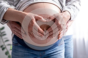 close up hands on mother and father making heart on pregnant big belly advanced pregnancy. Lover Parents waiting baby