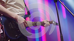 Close-up hands of musician playing an electric guitar on stage. Male musician with an electric guitar in his hands