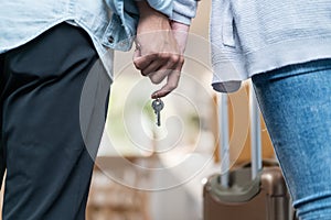 Close up hands of new marriage couple holding new house key together. Young attractive romantic man and woman holding suitcase