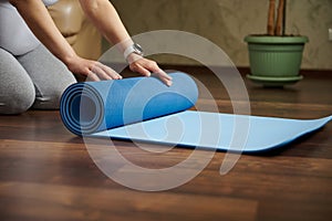 Close-up hands o pregnant woman rolling out a mat while practicing yoga, prenatal stretching, breathing exercises indoor