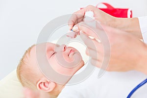 Pediatrician clearing the nose of a baby by applying saline solution photo