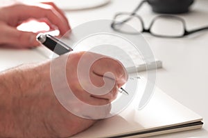 close-up of hands of person taking noted on paper white typing on computer keyboard