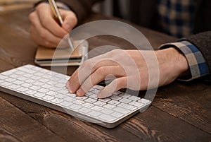 close-up of hands of person taking noted on paper white typing on computer keyboard.