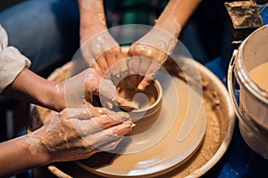 Close-up of the hands of a Potter`s girl and a child who are sculpting clay dishes on a Potter`s wheel.