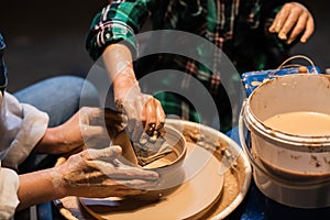 Close-up of the hands of a potter`s girl and a child who are sculpting clay dishes on a potter`s wheel.