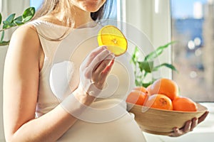 Close-up of hands of pregnant woman holding oranges in bowl, orange slice