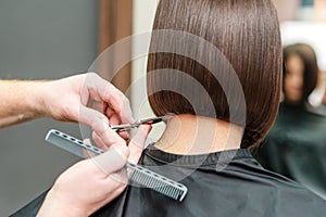 Close up hands of professional hair stylist are making short hair with scissors and comb