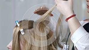 Close up of the hands of a professional hairdresser doing a curly hairstyle using a curling iron. The artist creates a