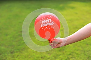 Close-up of hands with red balloon, green grass lawn meadow field as background in nature park forest outdoor outside sunset