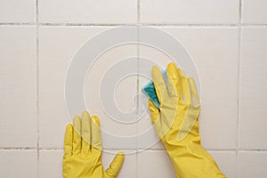 Close up of hands in rubber protective yellow gloves cleaning the white surface with a rag. Home, housekeeping concept