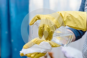 Close up of hands in rubber protective yellow gloves cleaning the white surface with a rag. Home, housekeeping concept