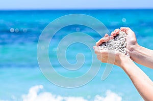 Close-up hands with sand in shape of heart against tropical turquoise sea