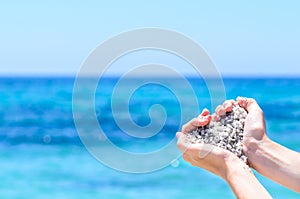 Close-up hands with sand in shape of heart against tropical turquoise sea