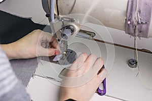 Close-up of the hands of a seamstress sewing clothes, sews fabric behind a sewing machine