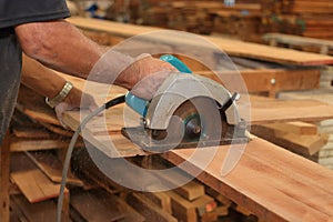 Close up hands of senior carpenter cutting a piece of wood against electric circular saw in carpentry woodshop. Woodworking concep