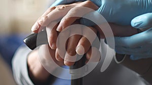Close-up of the hands of a senior citizen holding a walking stick, The hands of a medic in gloves shake hands with an elderly man.