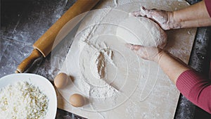 Close-up hands of senior female is kneading a dough at home kitchen, above view
