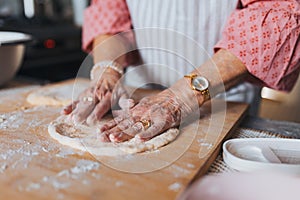 Close up of hands of senior woman preparing traditional easter meals for family, kneading dough for easter cross buns