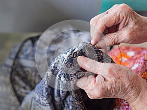 Close-up of hands senior woman using needle and thread to mend a pant. Selective focus. Concept of aged people and handmade