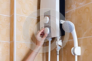 Close-up of hands setting the temperature of water in electric boiler in the shower room.