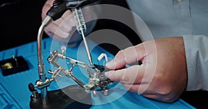 A close-up hands is soldering the video transmitter chip from an FPV drone.