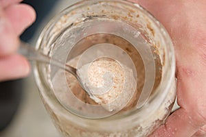 Close up of hands with a spoon grabbing part of sourdough starter