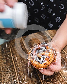 Close-up of hands sprinkling confectioners sugar on pastel de nata, Portuguese custard tart photo