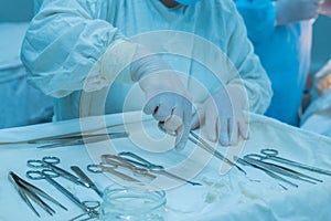 Close-up, hands of a surgical nurse taking medical instruments from a sterile table, against the background of a team of doctors