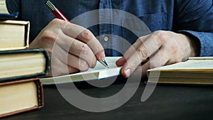 Close-up of hands taking notes in a notebook. A man is studying and reading the book in the library.
