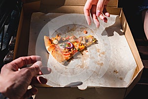 Close-up of hands taking a slice of pizza from a box. The concept of fast food, food delivery and lunch in nature