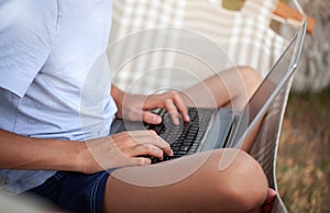 Close up hands teenager man workes on a laptop is sitting in hammock. Boy on summer vacation in nature. Concept distant work,