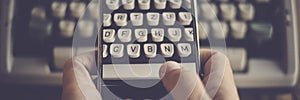 Close up of hands texting and writing on an old typewriter keyboard on modern mobile phone. Concept of technology and life in