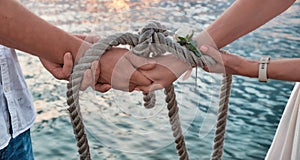 Close-up. Hands tied with sea rope against backdrop of sea water at sunset. An oath with hands as sign of eternal