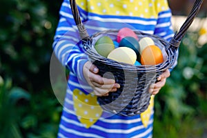 Close-up of of hands of toddler holding basket with colored eggs. Child having fun with traditional Easter eggs hunt