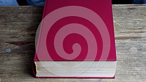 Close-up of the hands of two men and a woman folded in a prayer gesture on a thick family bible in a dark red cover, the concept