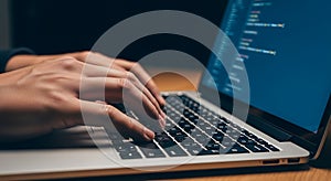 Close up of hands typing on a laptop keyboard with code visible on the screen in a dark room