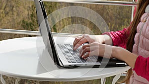 Close-up of hands typing on a laptop keyboard. teenager girl typing, working on laptop, in open balcony. spring sunny