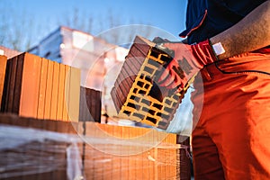 Close up on hands of unknown man construction worker taking clay brick orange hollow clay block for building at warehouse or