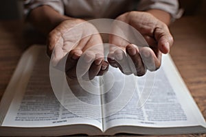 close up on the hands of an unrecognizable black woman reading the bible and praying.