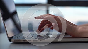 Close-up hands of unrecognizable business woman closing lid of laptop computer at desk on background of window