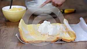 Close up hands of unrecognizable confectioner spreading cream on sponge cake when making swiss roll at home.