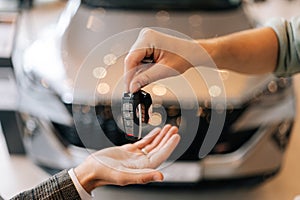 Close-up hands of unrecognizable dealer male giving new car key to customer man in business suit on blurred background