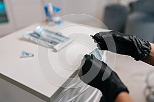 Close-up hands of unrecognizable female dentist in rubber gloves opening package with new nozzle for polishing and