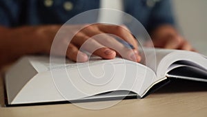 Close-up hands of unrecognizable man turning pages of reference book, slow motion, blurred background.